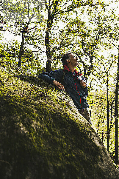 Nachdenklicher Mann steht vor einem Baum neben einem Felsen