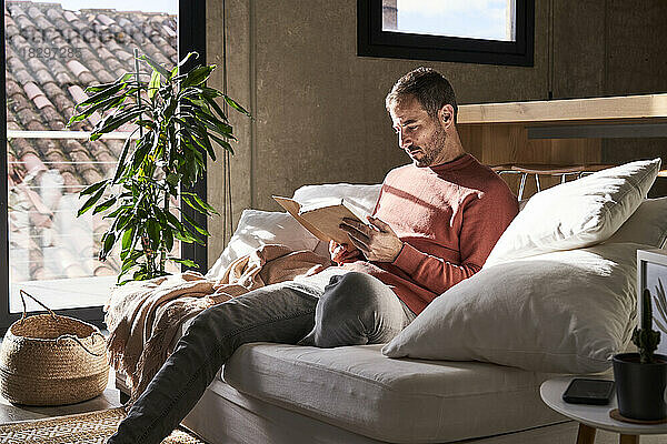 Mann sitzt zu Hause auf dem Sofa und liest ein Buch