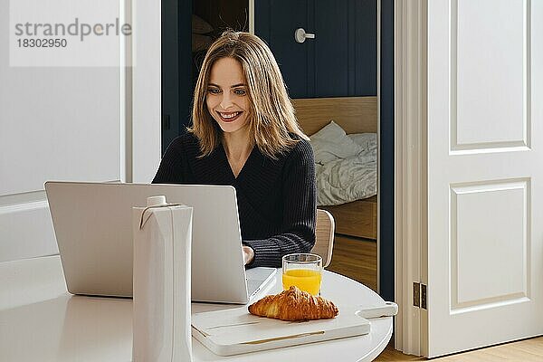 Glückliche lächelnde Frau  die von zu Hause aus mit ihrem Laptop online chattet