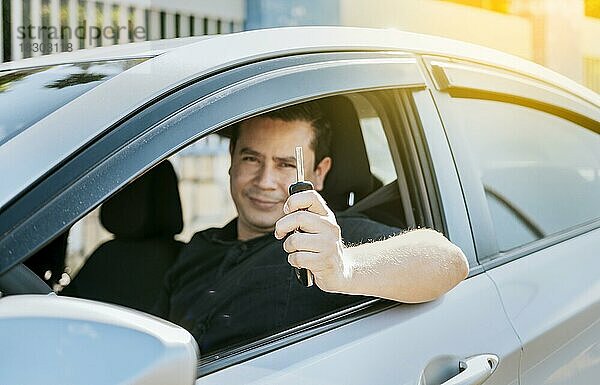 Glücklicher Mann zeigt seine neuen Autoschlüssel  Person in seinem Fahrzeug zeigt seine Autoschlüssel  Zufriedener Autokäufer Konzept  Fahrer in seinem Auto zeigt die Schlüssel aus dem Fenster