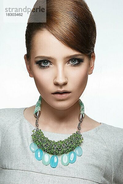 Schönes modisches Mädchen mit glattem Haar und originellem Schmuck um den Hals. Modell in Weiß. Schönes Gesicht. Bild im Studio auf einem weißen Hintergrund genommen