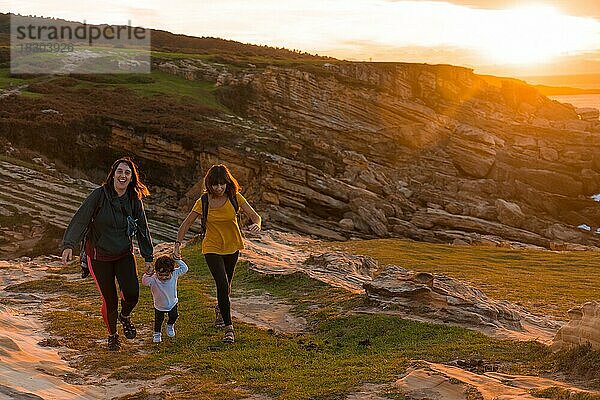 Zwei Schwestern mit einem Kind beobachten den Sonnenuntergang an der Küste am Meer  Familie Lebensstil