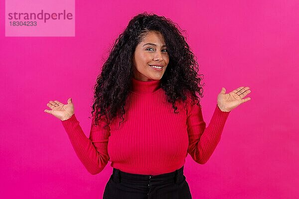 Lächelnde Frau mit lockigem Haar posiert auf einem rosa Hintergrund  Studioaufnahme  Lifestyle