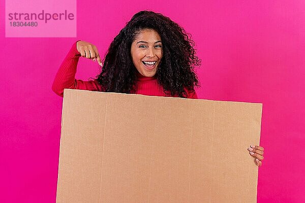 Lockenköpfige Frau  die auf ein Schild vor einem rosa Hintergrund zeigt  Studioaufnahme