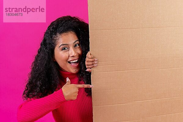 Lockenköpfige Frau  die auf ein Schild zeigt  lächelnd auf einem rosa Hintergrund  Studioaufnahme