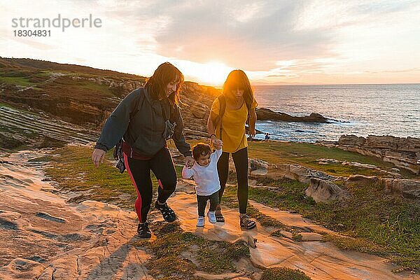 Lgbt Paar von Frauen mit einem Kind bei Sonnenuntergang an der Küste am Meer  Familie Lebensstil