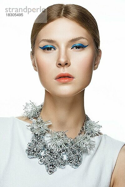 Schönes modisches Mädchen mit glattem Haar und originellem Schmuck um den Hals. Modell in Weiß. Schönes Gesicht. Bild im Studio auf einem weißen Hintergrund genommen