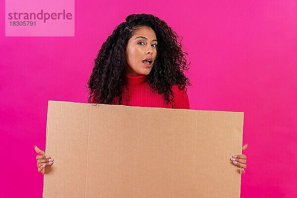 Lockenköpfige Frau hält ein Schild vor einem rosa Hintergrund  Studioaufnahme