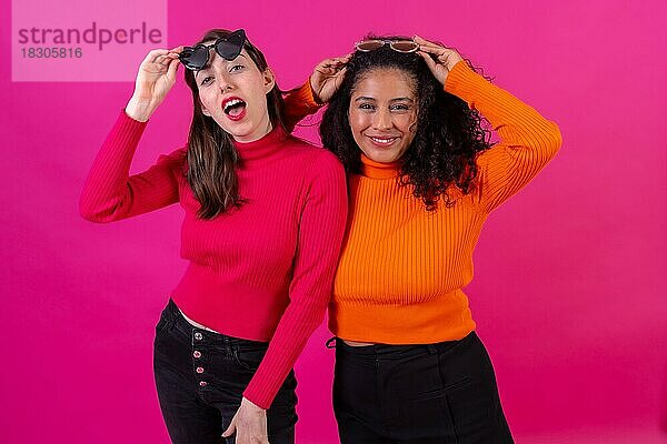 Portrait Freundinnen mit Sonnenbrille  die sich auf einem rosa Hintergrund amüsieren  Studioaufnahme  Lifestyle