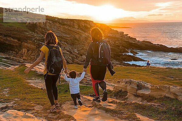 Lgbt Paar von Frauen mit einem Kind zu Fuß in den Sonnenuntergang an der Küste am Meer  Familie Lebensstil