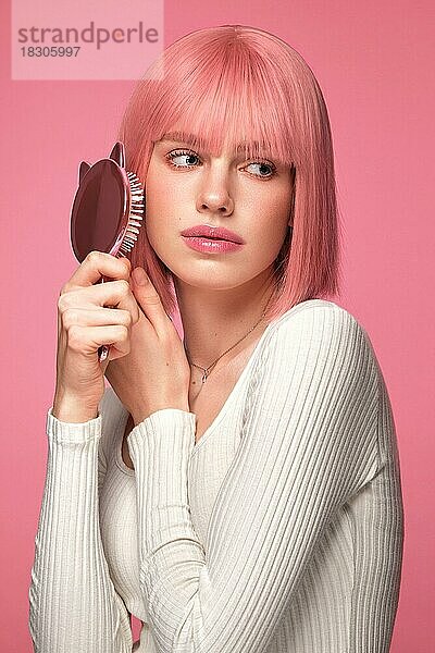 Schöne lustige niedliche Frau in rosa Perücke und klassischen Make-up. Das Porträt wurde in einem Studio vor einem rosa Hintergrund aufgenommen. Schönheit Gesicht