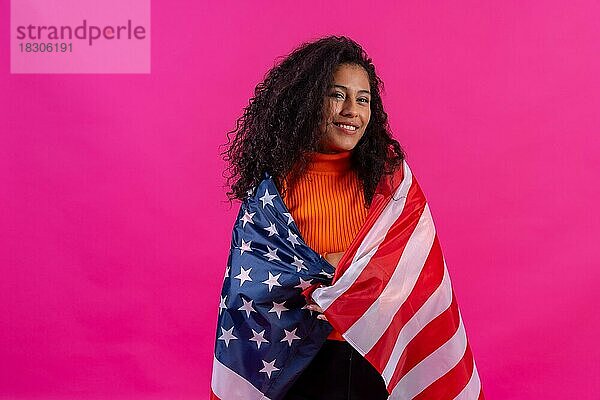 Lockenköpfige Frau umarmt usa-Flagge auf einem rosa Hintergrund  Studioaufnahme