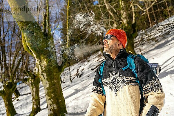 Ein Mann raucht eine Zigarette auf einem verschneiten Hügel im Winter und genießt das kalte Rauchen