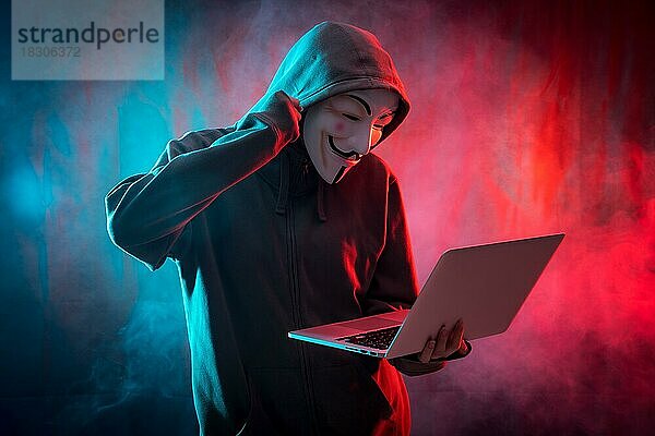 Hacker mit einer anonymen Maske mit einem Computer und machen einen Kampf Symbol  mit einem Hintergrund von Rauch und farbigen Leds