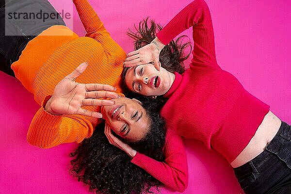 Zwei multiethnische Frauen machen im Liegen eine Stopp-Geste mit den Händen auf rosa Hintergrund