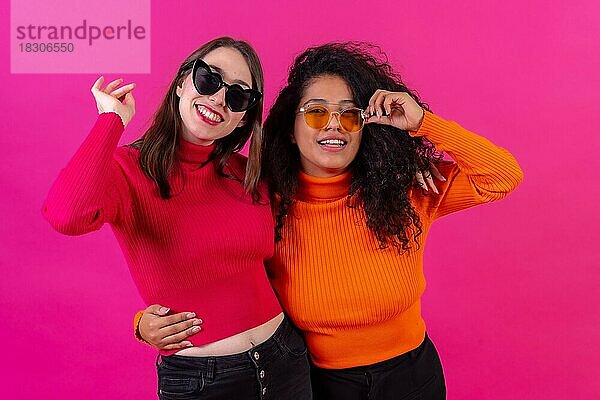 Weibliche Freunde mit Sonnenbrille  die Spaß haben und lächelnd auf einem rosa Hintergrund  Studioaufnahme  Lifestyle