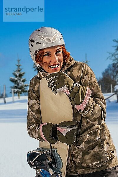 Frau mit Helm  in der Piste mit Snowboard stehend