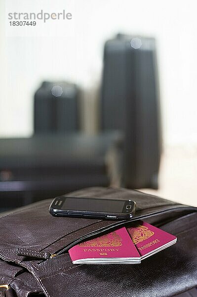 Pässe  die aus einer Reisetasche herausragen  mit Mobiltelefon  mit Gepäck dahinter. Auf einem Flughafen. Achten Sie auf Ihre Wertsachen und schützen Sie Ihre Dokumente