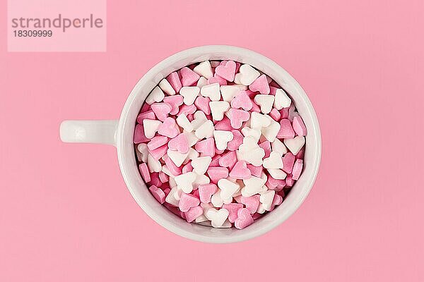 Draufsicht auf Teetasse gefüllt mit rosa und weißen Zuckerherzen auf rosa Hintergrund