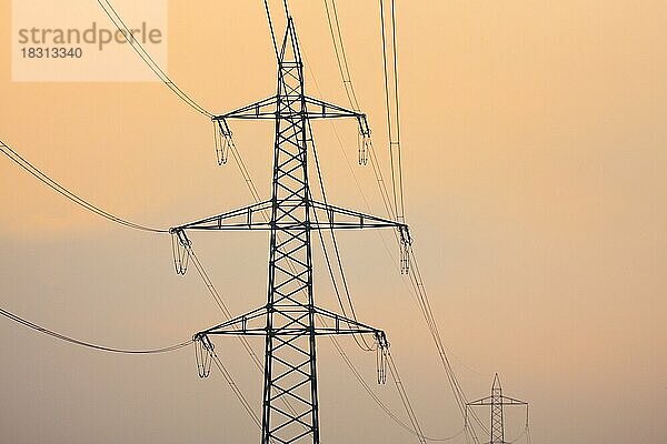 Silhouetten von Hochspannungsleitungs-Strommasten werden im Nebel in oranges Licht der untergehenden Sonne gehüllt  Kanton Zürich  Schweiz  Europa