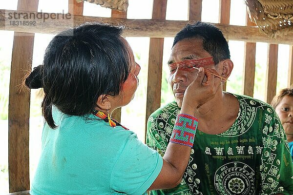 Indigenes Volk  Mann erhält von einer Frau eine traditionelle Gesichtsbemalung im Dorf der Ureinwohner Huni Kuin im Amazonas-Regenwald  Acre  Brasilien  Südamerika