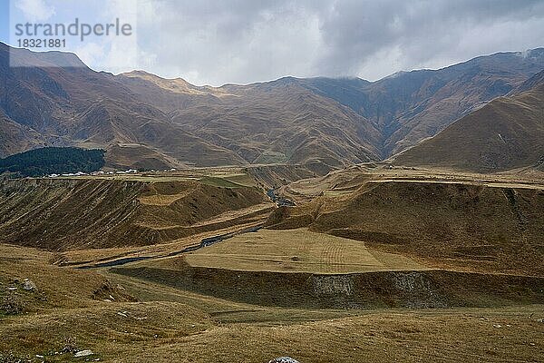 Hochgebirgslandschaft an der georgischen Heerstraße  Flussterrassen  zerschnitten von dem Fluss Kesia  der hier in den Fluss Terek mündet  links der Ort Kanobi  Distrikt Stepantsminda  Region Mtskheta-Mtianeti  Hoher Kaukasus  Georgien  Asien