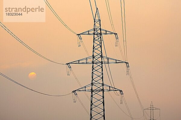 Untergehende Sonne hinter Silhouetten von Hochspannungsleitungs-Strommasten  inmitten von Nebel oranges Licht gehüllt  Kanton Zürich  Schweiz  Europa