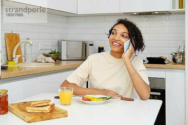 Glückliche attraktive afroamerikanische Frau  die während eines Telefonats beim Frühstück gute Nachrichten erhält