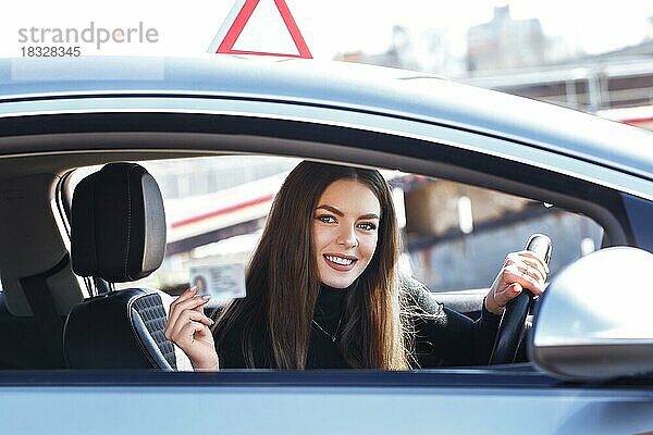 Fröhliches Mädchen  das mit einem Führerschein in der Hand einen Übungswagen fährt
