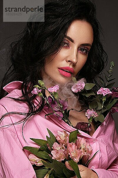 Schöne brünette Mädchen mit einem sanften rosa romantischen Make-up  rosa Lippen  hält Blumen. Die Schönheit des Gesichts. Porträtaufnahme im Studio