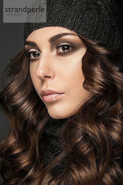 Schönes Mädchen mit Smokey-Make-up  Locken in schwarzer Winter-Strickmütze. Warmes Winterbild. Schönes Gesicht. Bild im Studio aufgenommen
