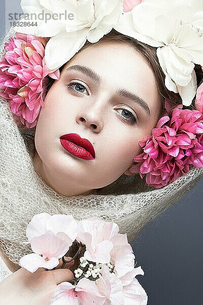 Schönes Mädchen mit einem Kopftuch im russischen Stil  mit großen Blumen auf dem Kopf und roten Lippen. Schönheit Gesicht. Bild im Studio auf einem grauen Hintergrund genommen