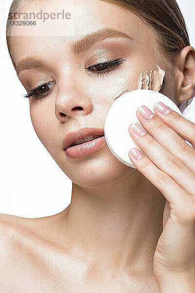 Schönes junges Mädchen mit Schwamm für die Anwendung Make-up und Französisch Maniküre. Schönheit Gesicht. Bild im Studio auf einem weißen Hintergrund genommen