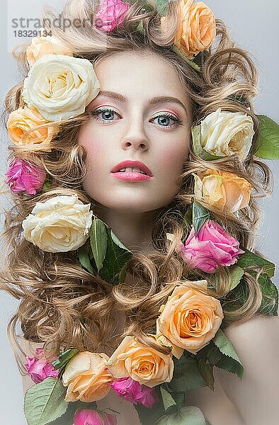 Schönes Mädchen mit vielen Blumen im Haar und leuchtend rosa Make-up. Frühling Bild. Schönheit Gesicht. Bild im Studio auf einem grauen Hintergrund aufgenommen