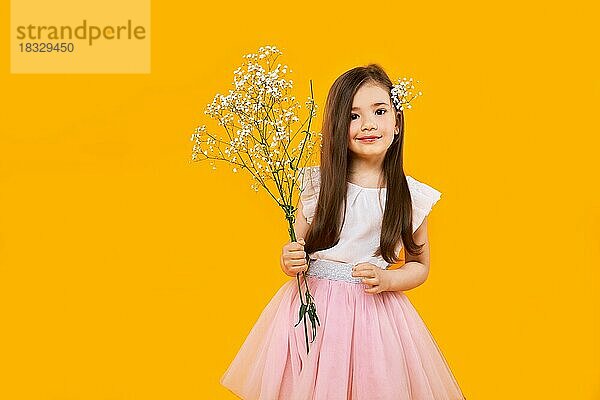 Nettes junges Mädchen mit Wildblumenstrauß in den Händen auf gelbem Hintergrund