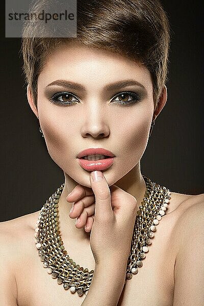 Schöne brünette Frau mit perfekter Haut  hellem Make-up und Goldschmuck. Schönes Gesicht. Bild im Studio auf einem grauen Hintergrund genommen