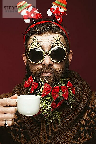 Lustiger bärtiger Mann in einem Neujahrsbild als Weihnachtsmann mit Dekorationen auf seinem Bart. Fest der Weihnacht. Fotos im Studio aufgenommen