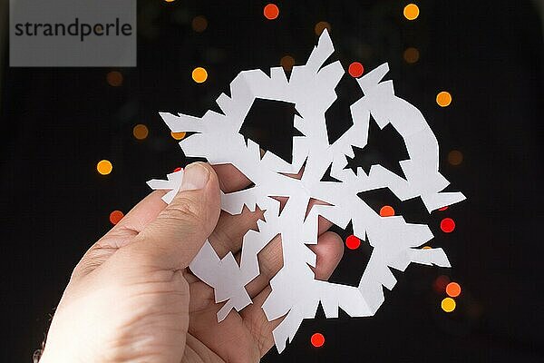 Schneeflocke geformt Papier in der Hand auf Bokeh Licht Hintergrund