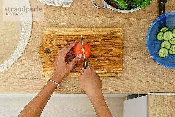 Draufsicht auf die Hände einer afroamerikanischen Frau  die eine Tomate für einen Salat schneidet