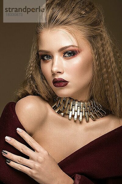 Schöne blonde Modell mit Locken  hellen Make-up  Goldschmuck und roten Lippen. Die Schönheit des Gesichts. Porträtaufnahme im Studio auf einem braunen Hintergrund