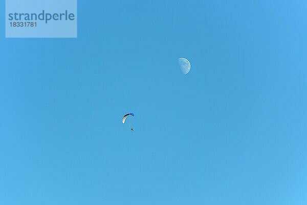 Paramotor im Flug an einem sonnigen Tag mit dem Mond am Himmel. Frankreich