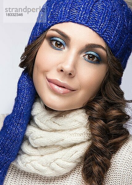 Schönes Mädchen mit sanftem Make-up  Locken und einem Lächeln in winterlicher blauer Strickmütze. Warmes Winterbild. Schönes Gesicht. Bild im Studio aufgenommen