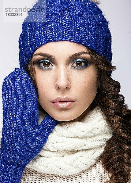 Schönes Mädchen mit sanftem Make-up  Locken und einem Lächeln in winterlicher blauer Strickmütze. Warmes Winterbild. Schönes Gesicht. Bild im Studio aufgenommen