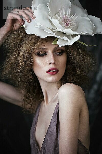 Schönes Mädchen mit lockigem Haar in Dessous mit großer Blume. Die Schönheit des Gesichts. Fotos im Studio geschossen