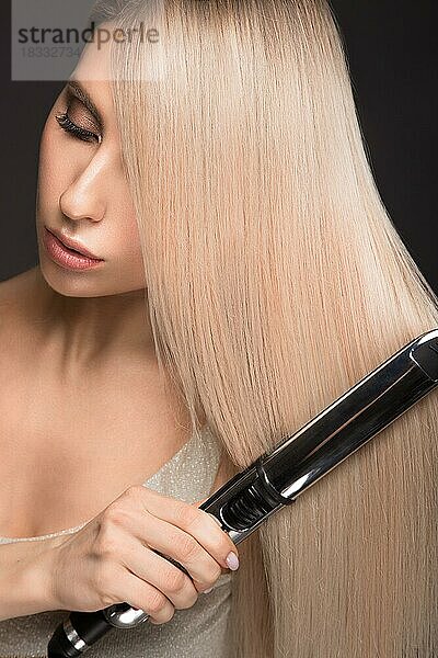 Schönes blondes Mädchen mit einem perfekt glatten Haar  klassisches Make-up mit Lockenstab in den Händen. Schönes Gesicht. Bild im Studio aufgenommen