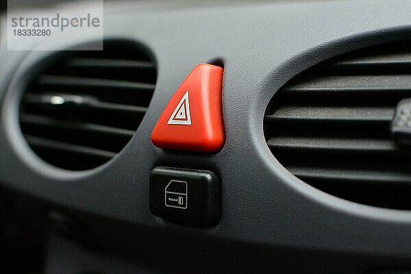Nahaufnahme eines dreieckigen roten Warnblinkerknopfes im Autoinnenraum