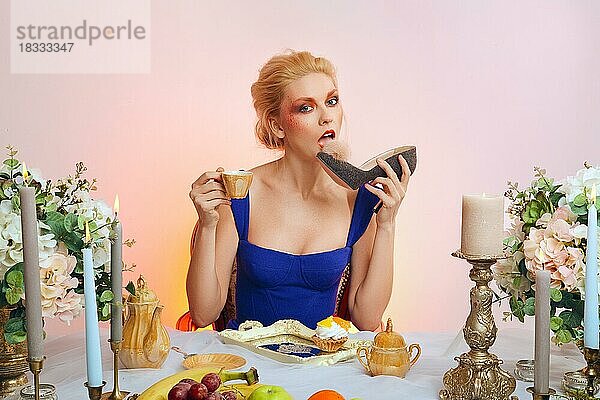Tricky Dame mit bunten Make-up sitzt hinter festlichen Tisch und Essen Filz Schuh