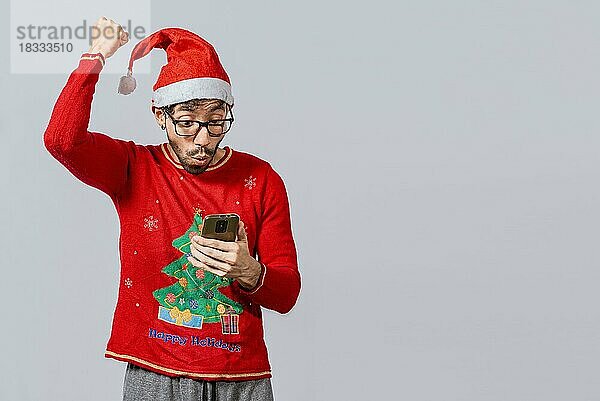 Menschen mit Weihnachtsmannmütze schauen aufgeregt auf ihr Handy  Aufgeregter junger Mann mit Weihnachtsmütze benutzt sein Handy beim Feiern  Aufgeregter Mann mit Weihnachtsmütze schaut auf sein Handy und feiert