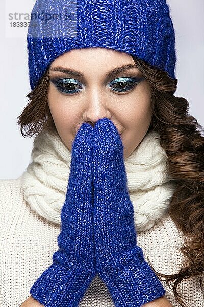 Schönes Mädchen mit sanftem Make-up  Locken und einem Lächeln in winterlicher blauer Strickmütze. Warmes Winterbild. Schönes Gesicht. Bild im Studio aufgenommen