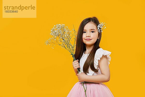 Nettes junges Mädchen mit Wildblumenstrauß in den Händen auf gelbem Hintergrund